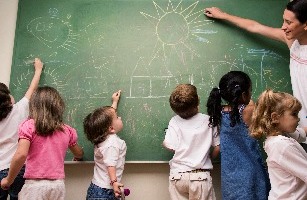 Young children and teacher drawing on a blackboard